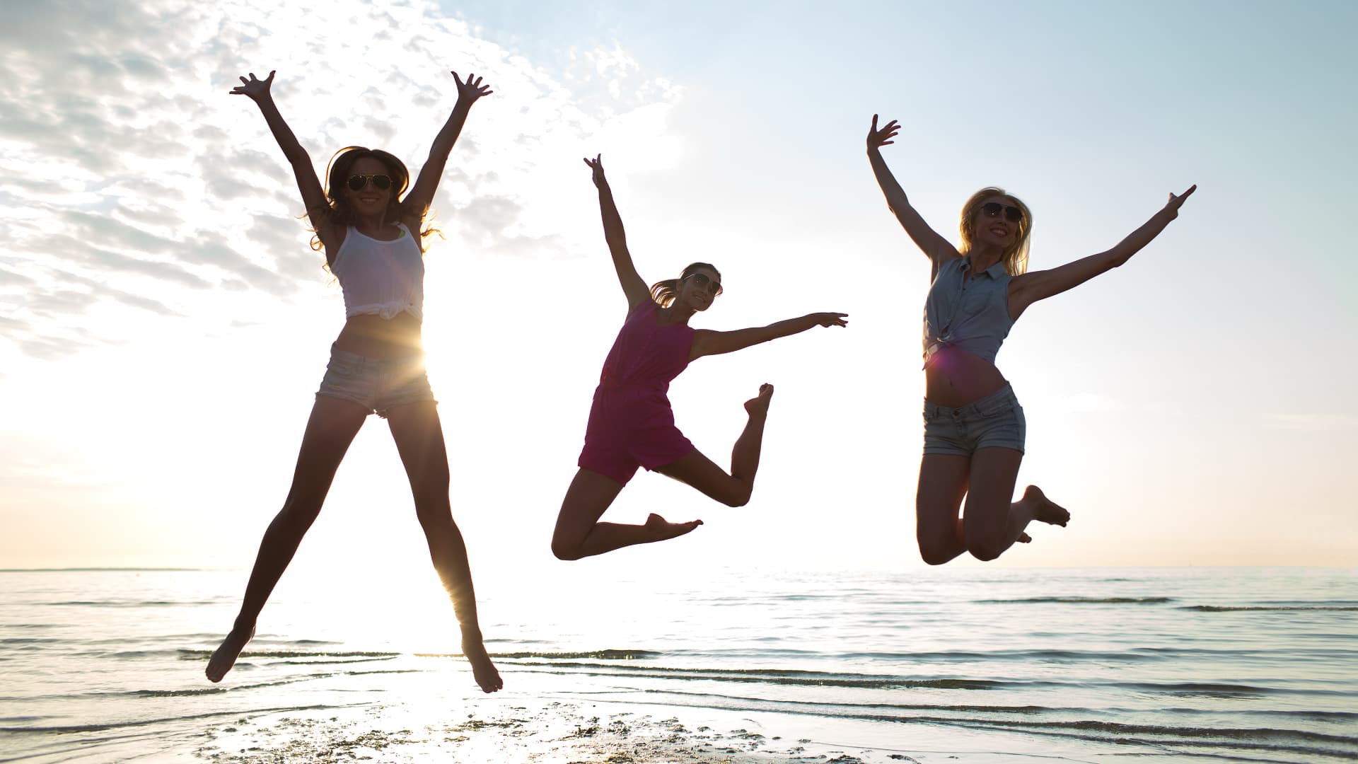 Three women joyfully jumping on the beach at sunset.