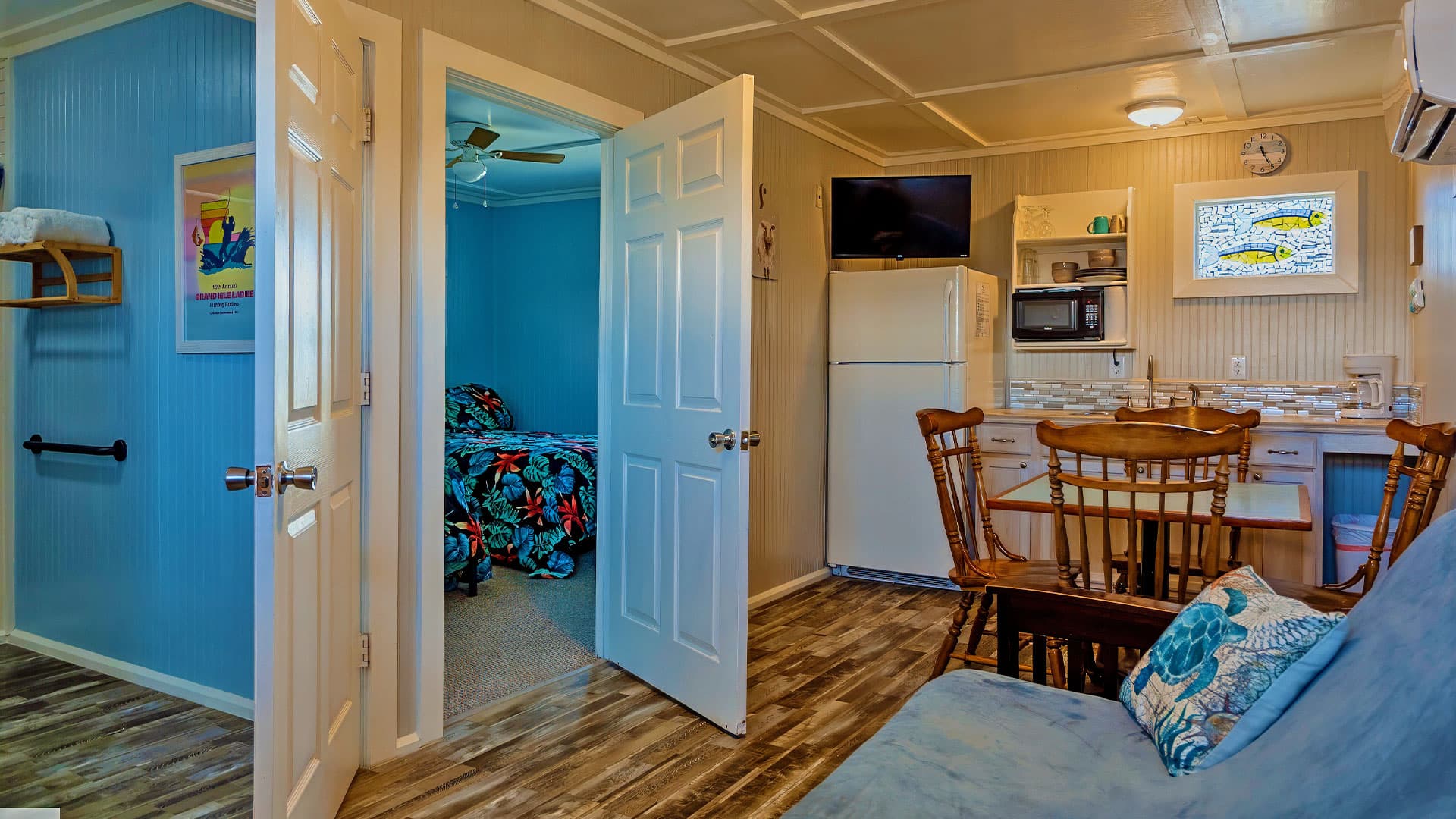 A cozy interior view of a light blue room with a kitchen, dining area, and an adjoining bedroom.