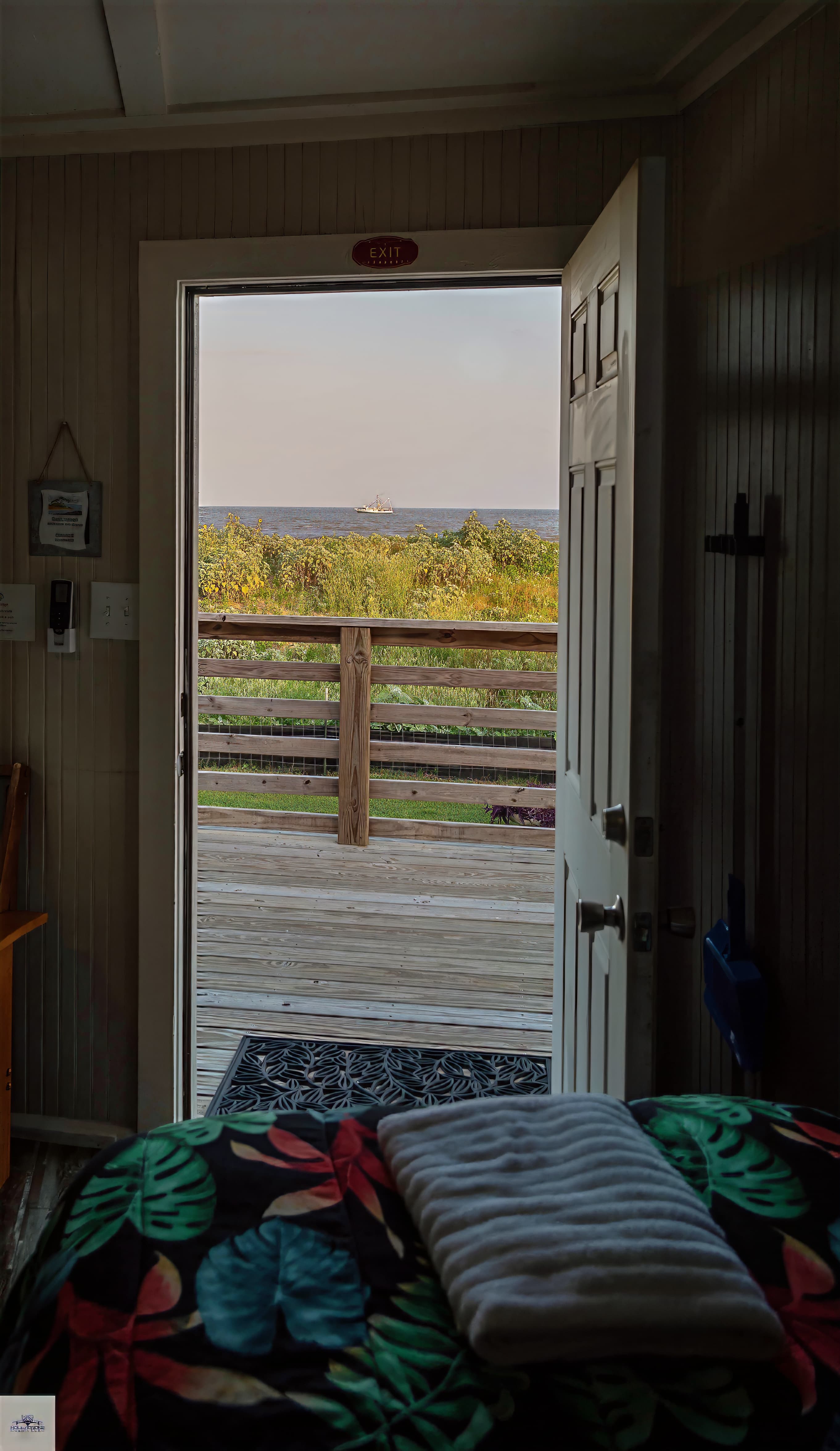 A view from a doorway looking out at a wooden deck and ocean with a distant boat.