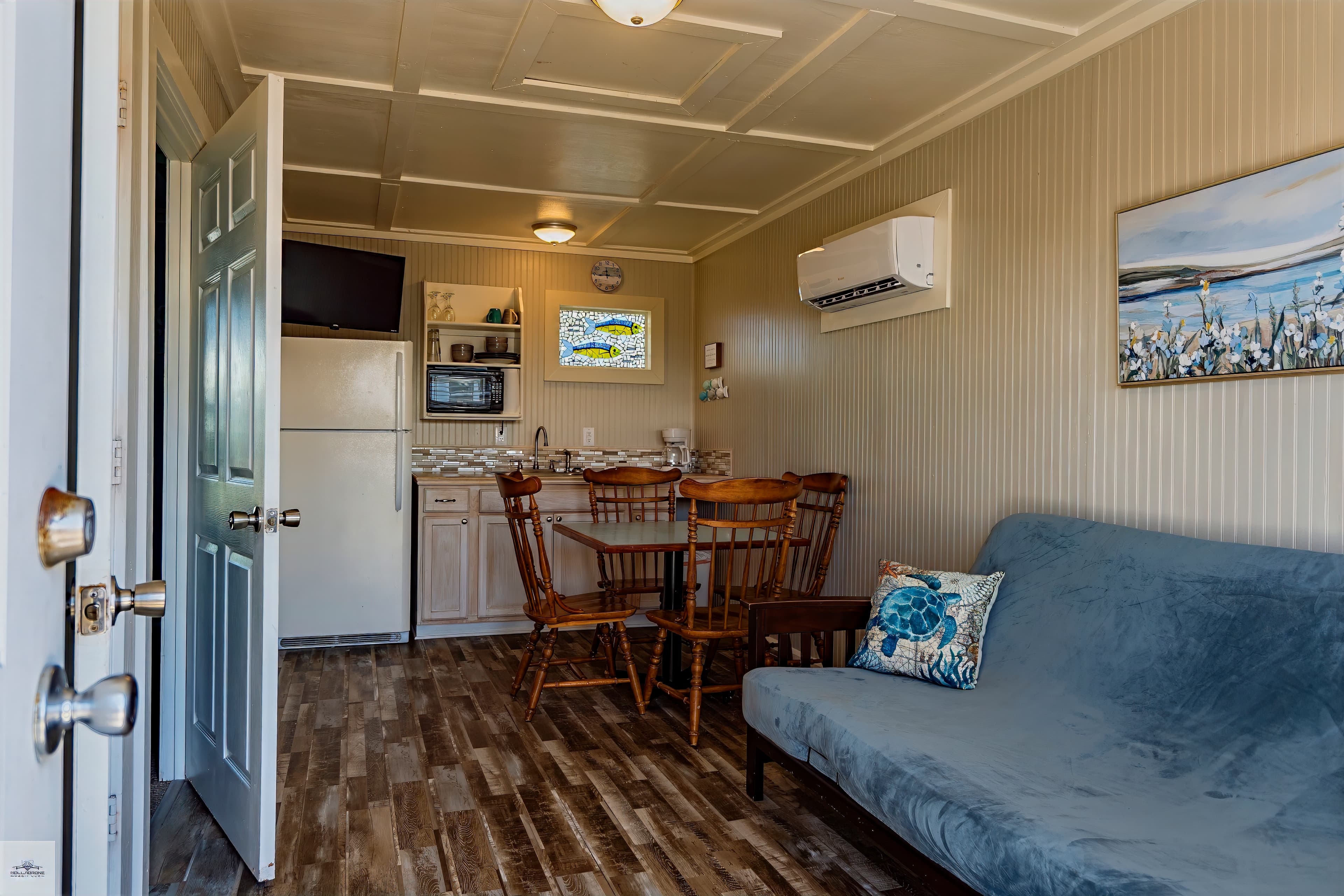 Junior suite interior with a blue futon, wooden dining table, and a compact kitchenette featuring a small fridge and microwave.
