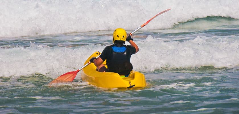 A person in a yellow kayak paddles through ocean waves.