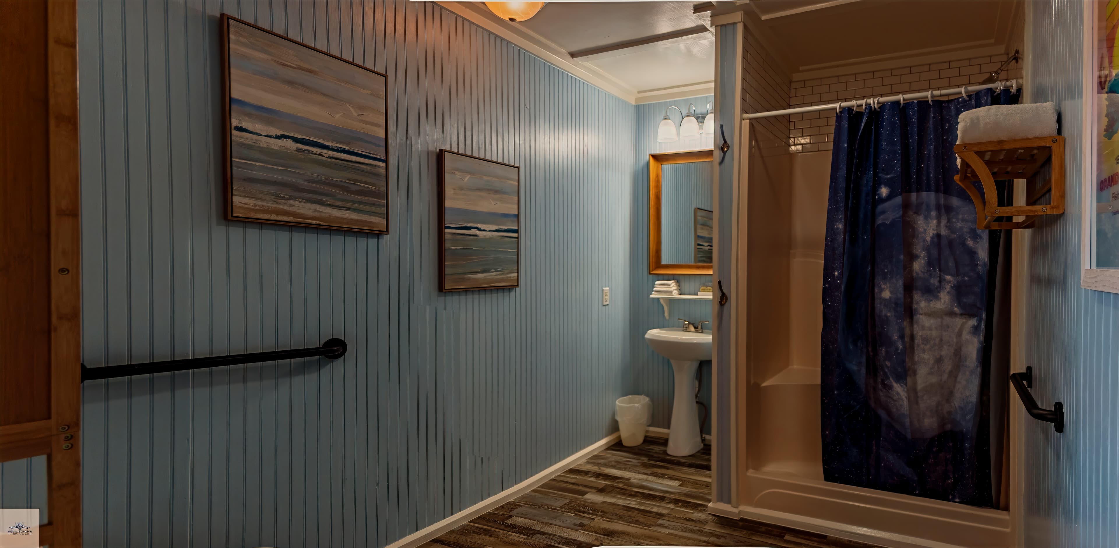 An accessible bathroom with light blue beadboard walls, a pedestal sink, and a white shower stall with a dark blue curtain.