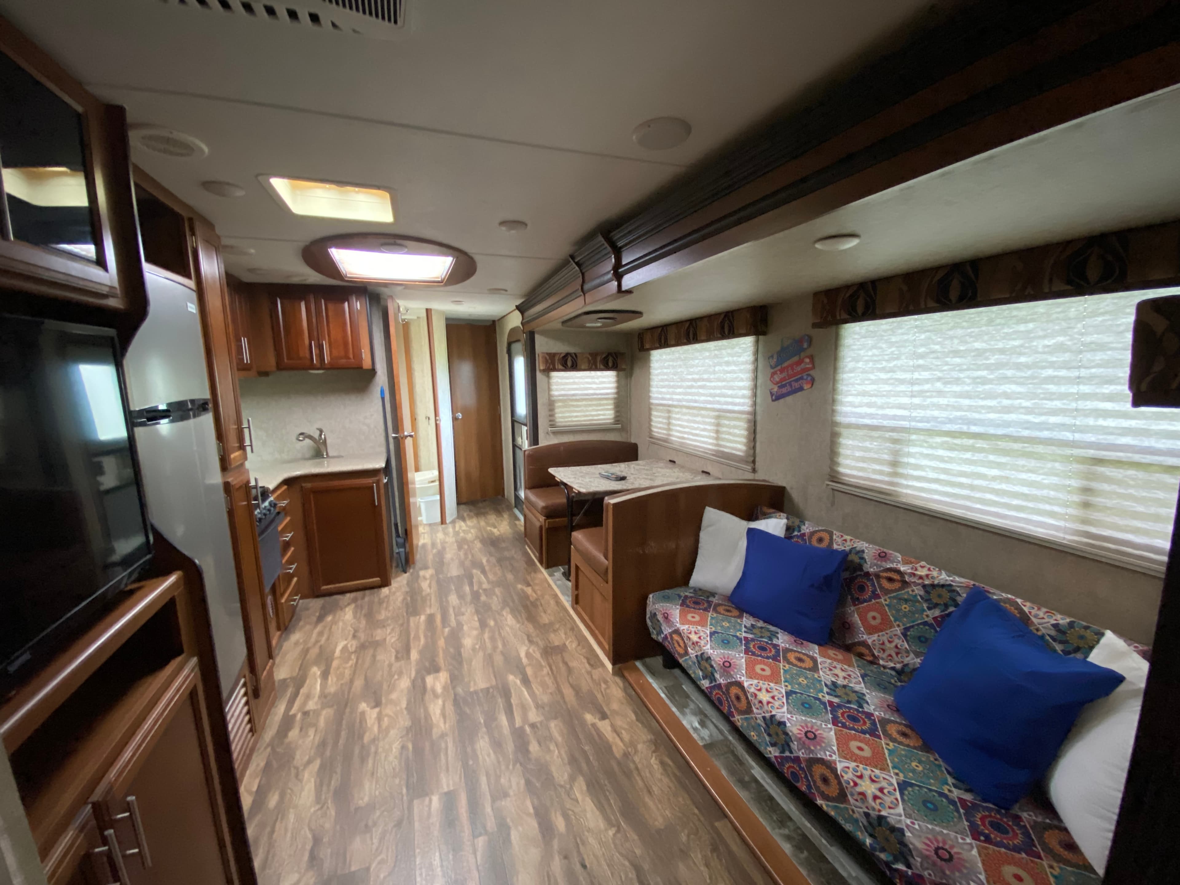 The interior of a camper with a narrow floorplan, showing a colorful sofa, brown dinette booth, and a compact kitchen with wood cabinetry.