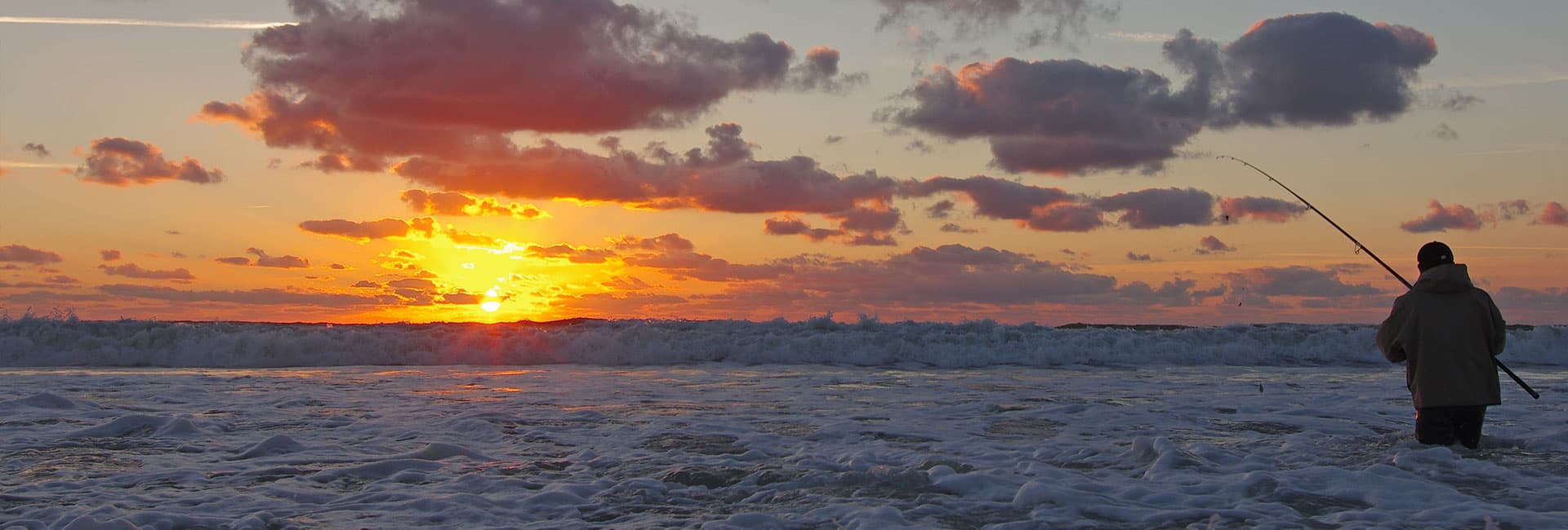 A person fishing in the ocean at sunset.