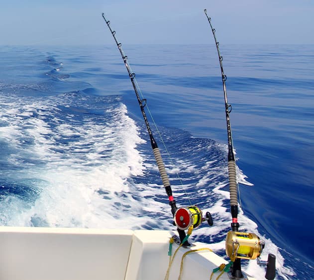 Two fishing rods with reels are positioned on the edge of a boat, trailing behind as it moves through calm blue waters.